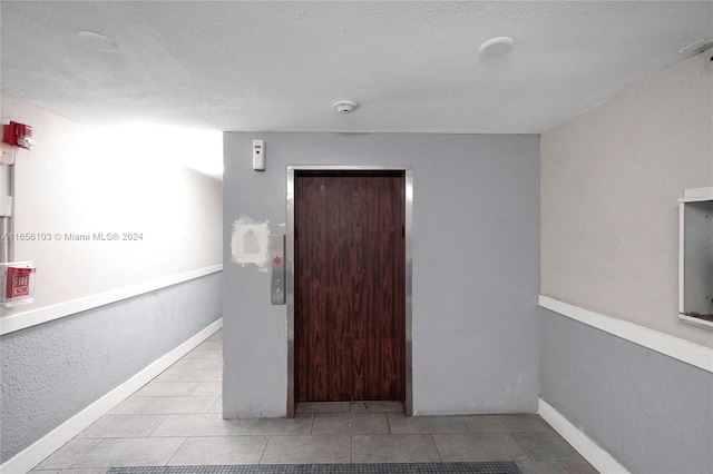 interior space featuring a textured ceiling, elevator, and light tile patterned floors