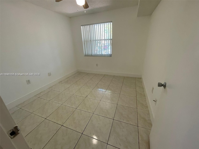 unfurnished room featuring a textured ceiling, light tile patterned floors, baseboards, and a ceiling fan
