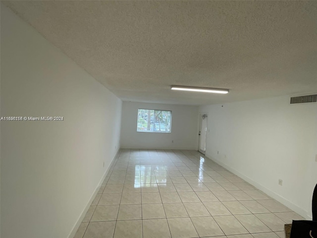 unfurnished room with visible vents, baseboards, light tile patterned floors, and a textured ceiling