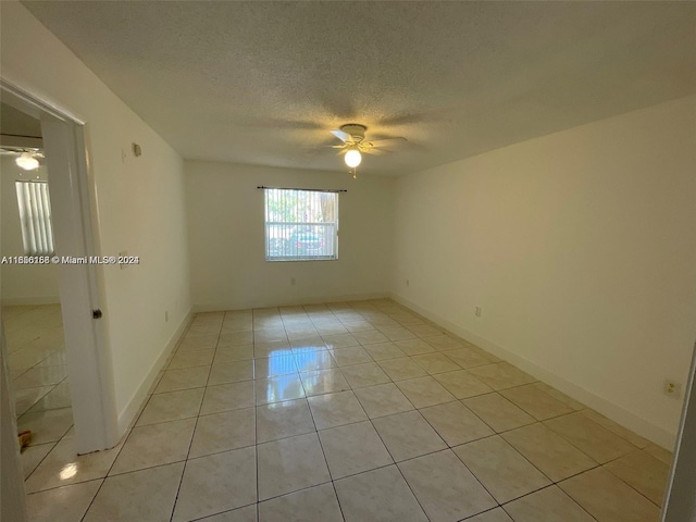 unfurnished room featuring a textured ceiling, light tile patterned floors, baseboards, and a ceiling fan