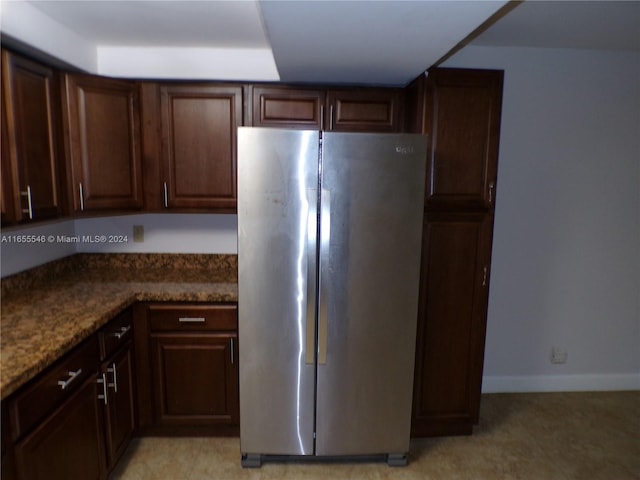 kitchen with dark stone counters, dark brown cabinetry, and stainless steel fridge