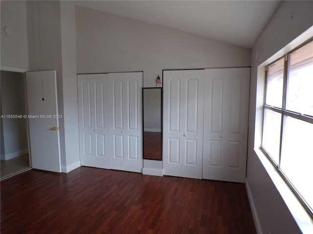 unfurnished bedroom featuring multiple closets, vaulted ceiling, and dark hardwood / wood-style flooring