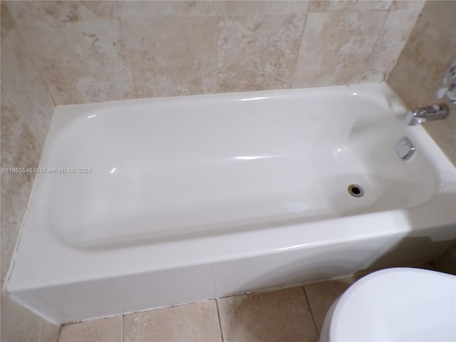 bathroom with a tub to relax in, tile patterned flooring, and toilet