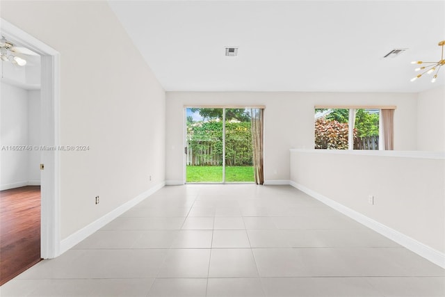 empty room featuring ceiling fan with notable chandelier, light tile patterned flooring, and a healthy amount of sunlight