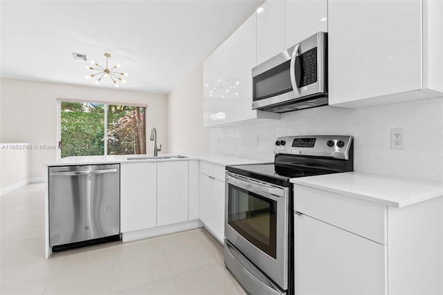 kitchen featuring white cabinets, appliances with stainless steel finishes, a notable chandelier, sink, and light tile patterned flooring