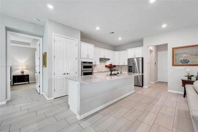 kitchen featuring light stone counters, a kitchen island with sink, white cabinets, decorative backsplash, and appliances with stainless steel finishes