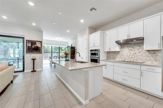 kitchen featuring white cabinets, sink, a kitchen island with sink, black electric cooktop, and stainless steel double oven