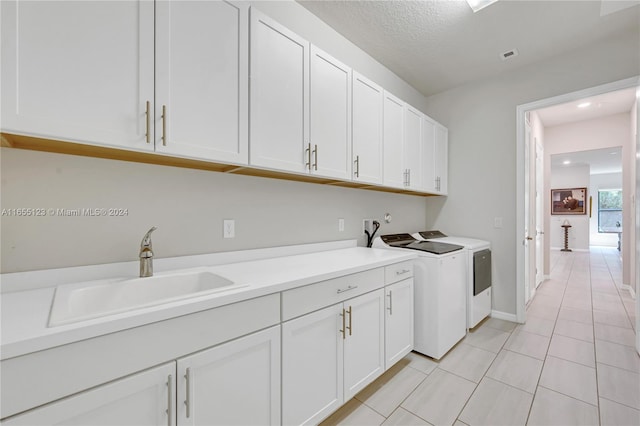 laundry room featuring light tile patterned floors, sink, a textured ceiling, cabinets, and washing machine and dryer