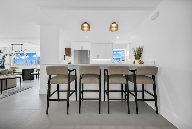 kitchen featuring a kitchen breakfast bar, stainless steel refrigerator, white cabinets, and a notable chandelier