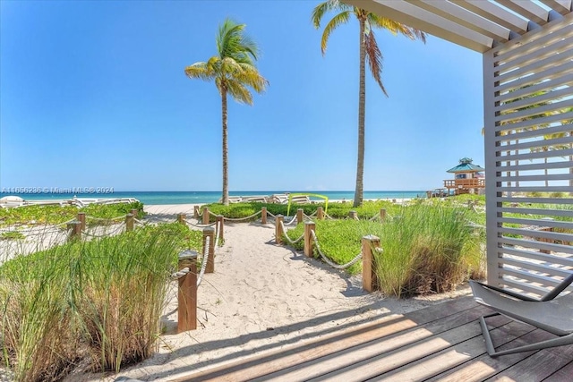 exterior space with a water view, a view of the beach, and a pergola