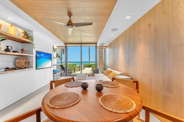 dining space with floor to ceiling windows, wood ceiling, wood walls, and ceiling fan