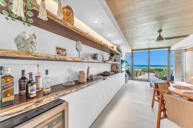 interior space with wooden ceiling, beverage cooler, a wall of windows, ceiling fan, and a water view