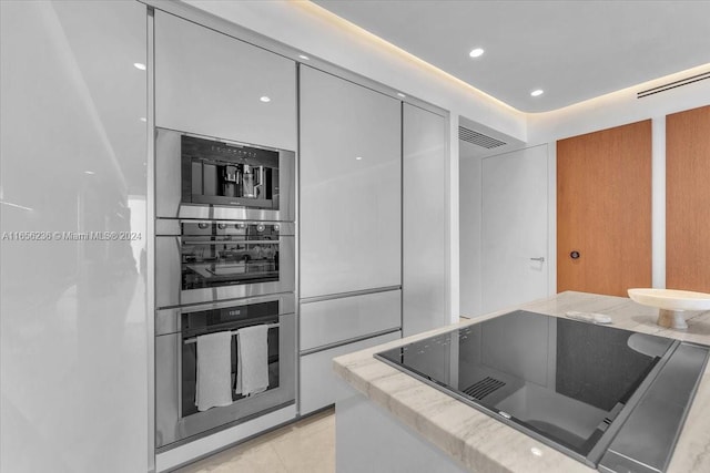 kitchen with stainless steel oven, black electric stovetop, light tile patterned flooring, and light stone countertops