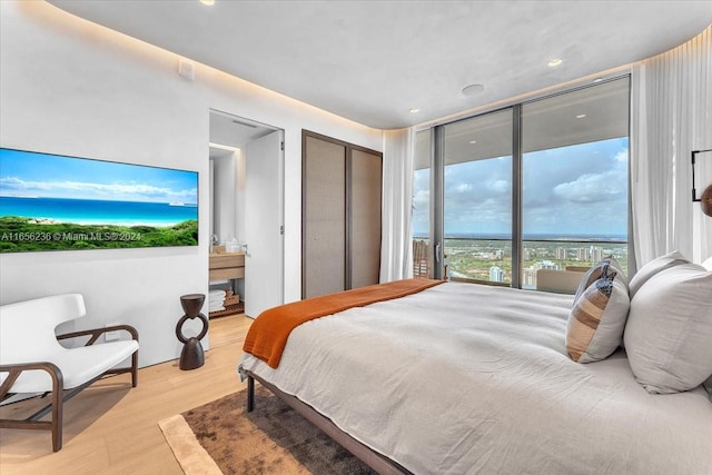 bedroom featuring connected bathroom, light wood-type flooring, a water view, and access to outside