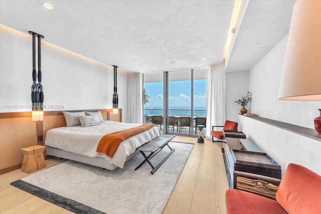 bedroom featuring wood finished floors, access to exterior, floor to ceiling windows, and a water view