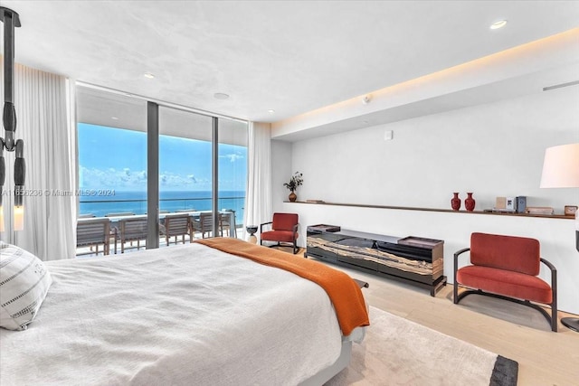 bedroom with a wall of windows, wood finished floors, visible vents, access to exterior, and a water view