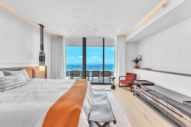 bedroom featuring light wood-type flooring, a water view, access to exterior, and a wall of windows