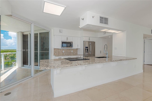 kitchen featuring a kitchen breakfast bar, light stone counters, sink, appliances with stainless steel finishes, and white cabinets