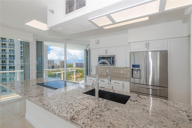 kitchen with appliances with stainless steel finishes, light stone counters, white cabinetry, and sink