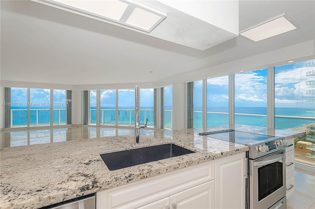 kitchen with stainless steel electric stove, sink, white cabinetry, light stone counters, and a water view