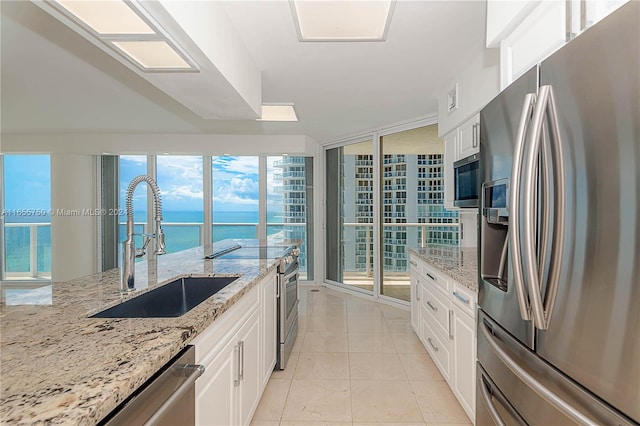 kitchen featuring light stone countertops, stainless steel appliances, sink, white cabinetry, and a water view