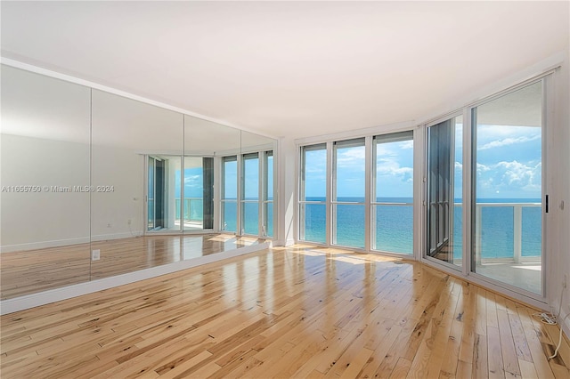 empty room featuring plenty of natural light, light hardwood / wood-style flooring, expansive windows, and a water view