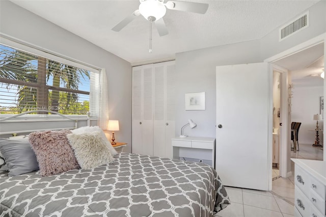 bedroom featuring a textured ceiling, light tile patterned floors, ceiling fan, and a closet