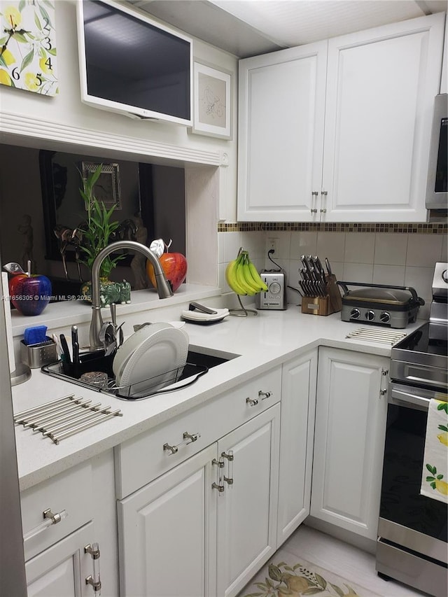 kitchen with stainless steel range with electric stovetop, white cabinetry, decorative backsplash, and sink