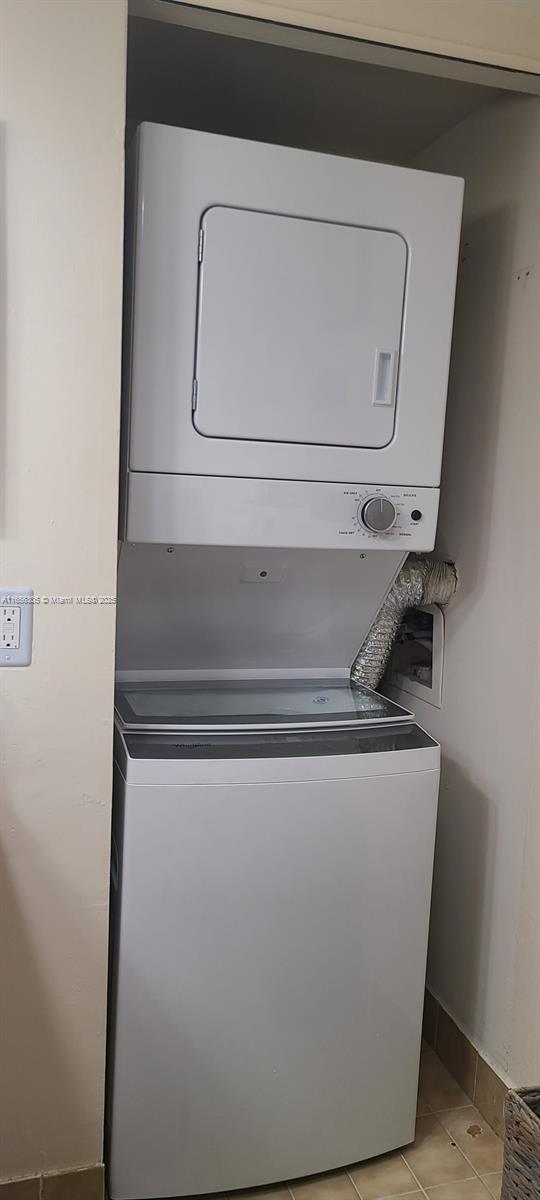 laundry room featuring stacked washer / drying machine and light tile patterned flooring