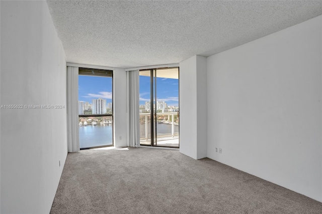 carpeted spare room featuring a water view, expansive windows, and a textured ceiling