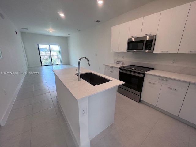 kitchen with light tile patterned floors, stainless steel appliances, a kitchen island with sink, and sink