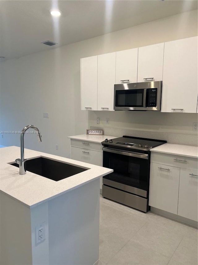 kitchen featuring light tile patterned floors, appliances with stainless steel finishes, light stone counters, white cabinetry, and sink