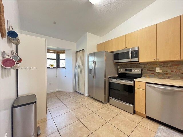 kitchen with light brown cabinetry, light tile patterned floors, stainless steel appliances, and vaulted ceiling