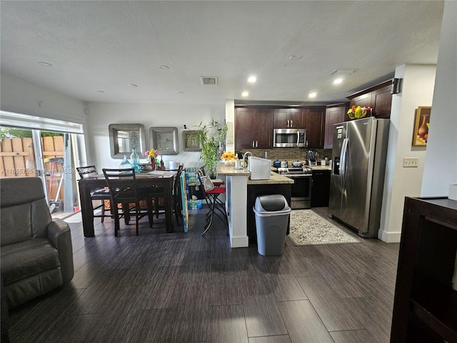 kitchen with a kitchen bar, stainless steel appliances, a kitchen island, light stone countertops, and dark brown cabinetry