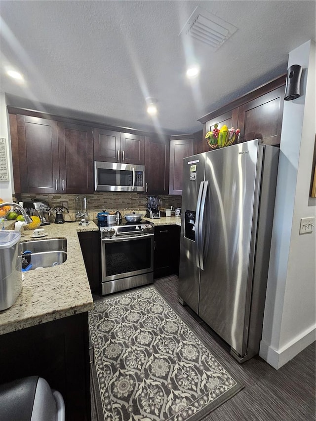 kitchen featuring light stone countertops, stainless steel appliances, sink, dark brown cabinets, and tasteful backsplash