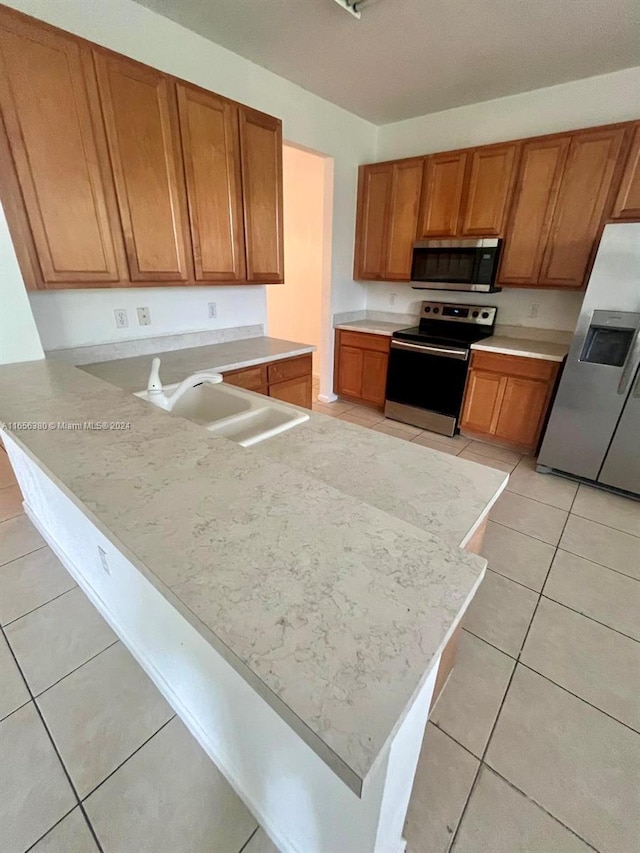 kitchen with kitchen peninsula, appliances with stainless steel finishes, light tile patterned floors, and sink