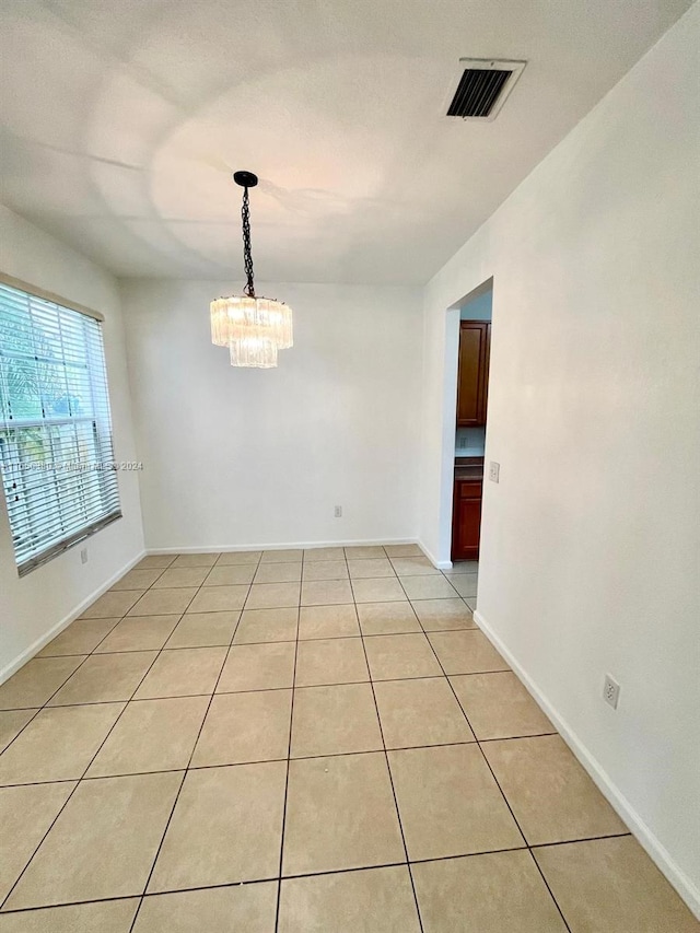 tiled spare room with a chandelier