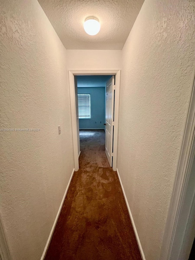 corridor featuring dark carpet and a textured ceiling