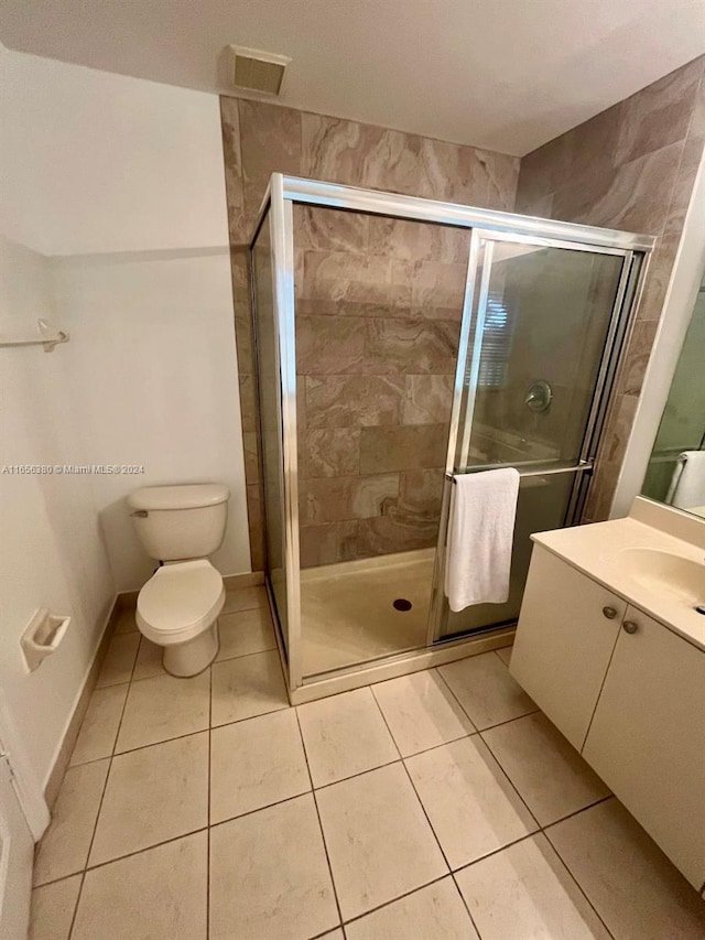 bathroom with tile patterned floors, a shower with door, vanity, and toilet