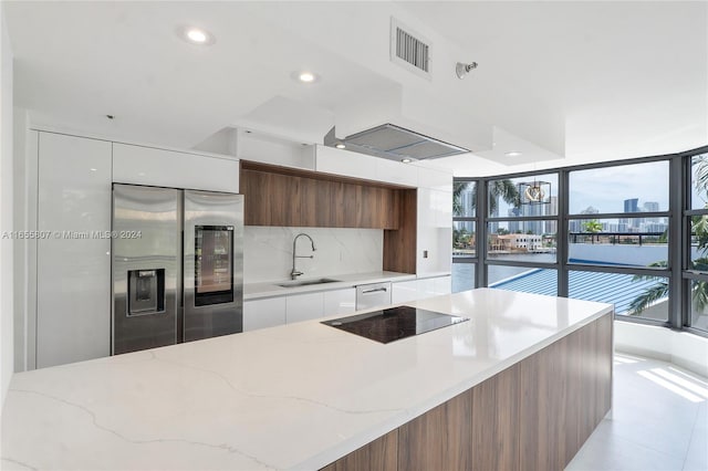 kitchen featuring white cabinets, light stone countertops, stainless steel built in fridge, and sink