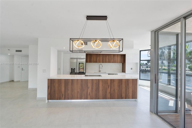 kitchen with stainless steel fridge, pendant lighting, tasteful backsplash, sink, and white cabinetry