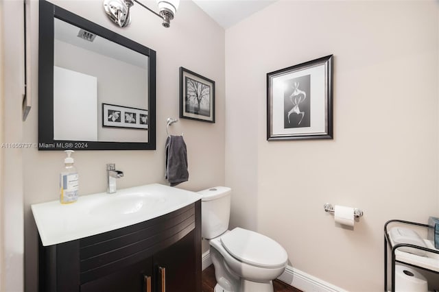 half bathroom with vanity, toilet, baseboards, and visible vents