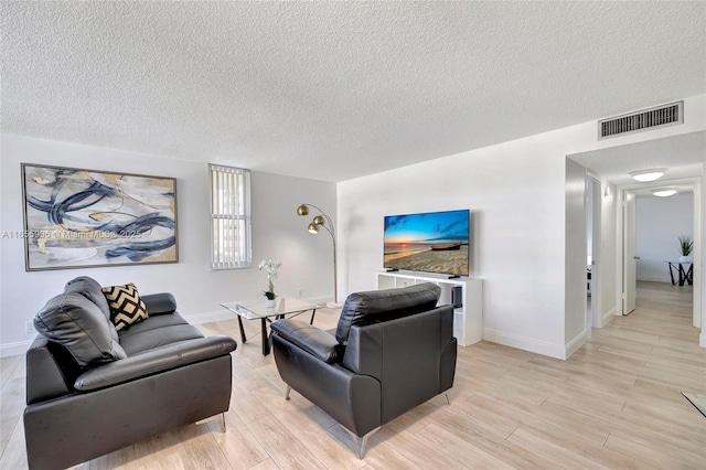 living area with light wood-type flooring, baseboards, visible vents, and a textured ceiling