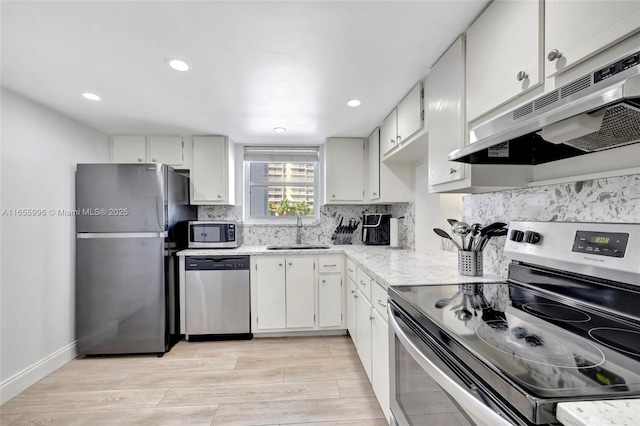 kitchen featuring appliances with stainless steel finishes, a sink, backsplash, and light wood finished floors
