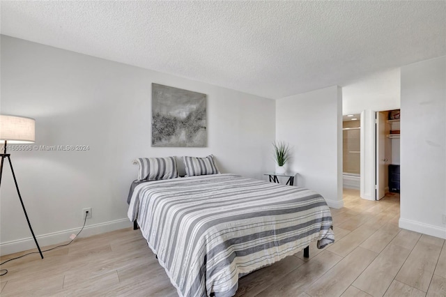 bedroom featuring a textured ceiling, ensuite bath, and light hardwood / wood-style floors