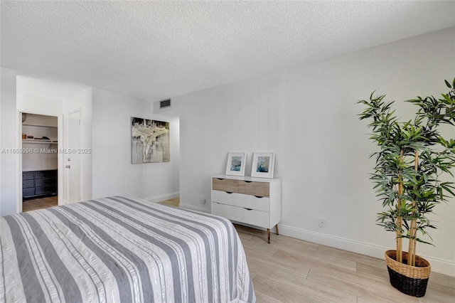 bedroom with light wood finished floors, baseboards, visible vents, and a textured ceiling