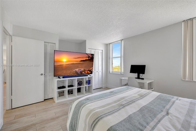 bedroom with light wood-style flooring, a textured ceiling, and two closets
