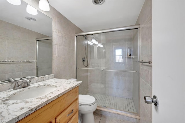 full bath with a stall shower, tile walls, toilet, and vanity