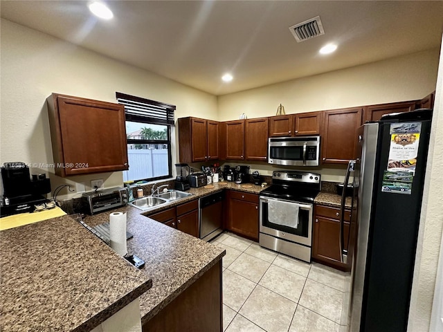 kitchen with appliances with stainless steel finishes, kitchen peninsula, sink, and light tile patterned flooring