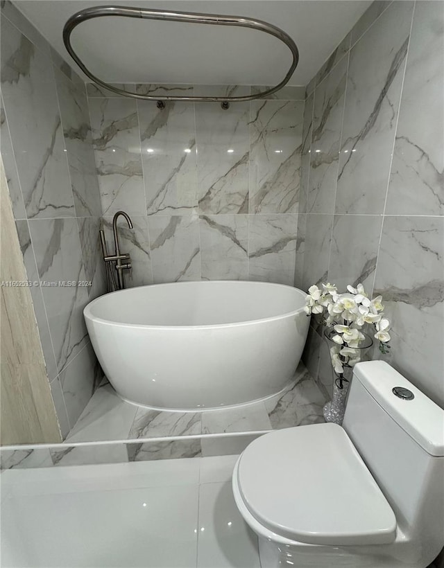 bathroom featuring marble finish floor, tile walls, a soaking tub, and toilet